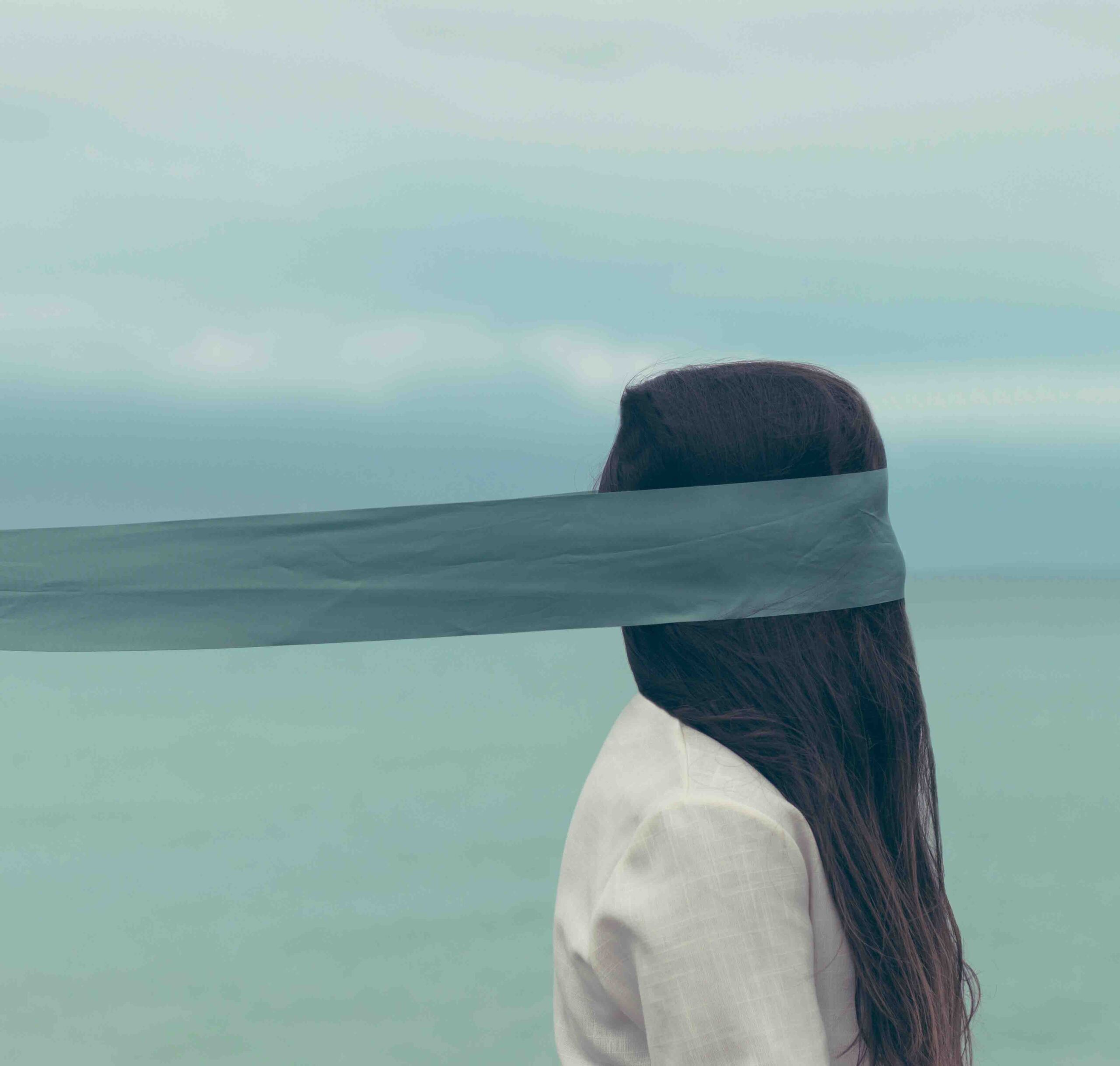 woman in front of a body of water with a piece of fabric covering her eyes
